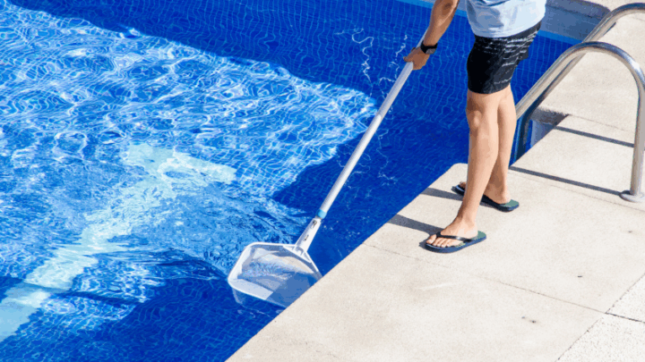 Man cleaning in-ground pool with a net.
